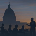 Twilight scene showing silhouettes of a presenter with an accessibility emblem and workshop attendees—including a person in a wheelchair—seated with laptops before a darkened Capitol dome.